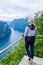 Tourist woman looks at Geirangerfjord and Seven Sisters Waterfall near small village of Geiranger. View from Eagles Road viewpoint