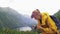 A tourist woman is making a photo of a beautiful mountain lake and green peaks in front of her and then she turns around