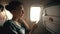 Tourist woman sitting near airplane window at sunset and using mobile phone during flight