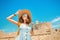 Tourist woman on vacation posing with hat and backpack in front of the old ruined fort and lighthouse in Rhodes, Greece