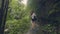Tourist woman walking on path in tropical forest on green trees and plant background. Back view traveling girl in exotic