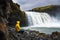 Tourist in a yellow jacket relaxing at the Godafoss waterfall in Iceland