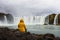 Tourist in a yellow jacket relaxing at the Godafoss waterfall in Iceland