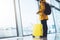 Tourist with yellow suitcase backpack is standing at airport on background large window, traveler man waiting in departure lounge
