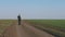 Tourist young male walking on a dirt road through a green field