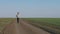 Tourist young male walking towards on a dirt road through a green field