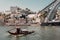 Touristic riverboat sailing past riverside and huge bridge over river Douro
