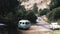 Tourists in cars navigate narrow road surrounded by mountains and lush greenery