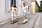 Tourists couple skateboarders riding skates. Happy young travelers longboarding together on sunset on pavement. Stylish man and