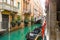 Tourists cross a bridge over a small canal with a gondola parked in the historic center of Venice Italy