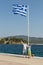 Tourists father and daughter near Greek flag on the Aegean coast of Sithonia peninsula