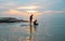 Tourists paddle surfboards in the sunset on a day when the sea has little waves