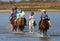 Tourists people and cowgirl riding horses in water