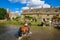 Tourists riding horses crossing the river in Lower Slaughter, a village in Cotswolds area, England, UK