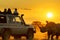 tourists in safari vehicle watching rhino at sunset