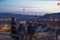 Tourists sitting on bench at top of hill taking pictures of hot air balloons flying over Cappadocia at night. Colorful