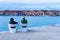 Tourists sitting on white chairs viewing the blurred industrial shipyard along the sea in Venice, Italy