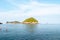 Tourists are snorkeling in the ocean with rocks with vegetation underneath beautiful blue sky with clouds