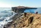 Tourists stand on a rock and look at the  Cape Tobizin, a scattering of rock fragments covered with snow and ice floes floating in