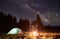 Tourists standing around campfire in night forest.