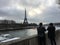 Tourists take photos of Eiffel Tower across the Seine on a cloudy winter day