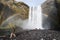 Tourists taking photos of waterfall Skogafoss, rainbow around them, Iceland