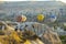 Tourists on top of hill watching hot air ballons flying over mountain landscape of Cappadocia during daytime. Horizontal
