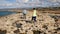 Tourists walk along the sharp loose limestone coast along the sea.