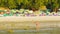 Tourists walk on a Kamala beach on low tide time with beach umbrellas shairs and beds on backgroun