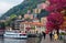 Tourists walk on a lakeside promenade under beautiful blossoming trees by Lake Como in Lombardy Italy