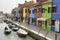 Tourists walking on colorful streets of Burano city with boats and traditional houses near lagoon