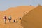 Tourists walking up a red dune in Sossuslvei, Namib Naukluft National Park, Namib desert, Namibia