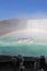 Tourists watch Niagara Falls tour boat under a full rainbow vert