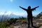 Tourists Woman in a sweater standing on the cliff, with raised hands and looking to sky and mountain