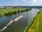 Towboat pushes barge with sand along calm river past fields