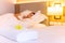 Towel with flower on bed in hotel room with woman sleeping in background.