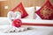 Towels folded in bird shape with pink flowers on the white bed in the bedroom with wood headboard and red Chinese style pillows