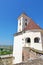 The tower of an ancient Ukrainian castle with a spire and a big clock on a tower in the background of a village with