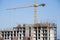 Tower crane constructing a new residential building at a construction site against blue sky. Renovation program, development,