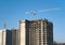 Tower crane constructing a new residential building at a construction site against blue sky. Renovation program, development,