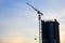 Tower crane lifting a concrete bucket at construction site on the against blue sky and sunset