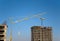 Tower cranes constructing a new residential building at a construction site against blue sky.