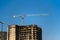 Tower cranes constructing a new residential building at a construction site against blue sky.