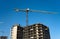 Tower cranes constructing a new residential building at a construction site against blue sky.