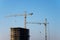 Tower cranes constructing a new residential building at a construction site against blue sky. Renovation program, development,