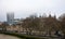 The Tower of London and The City with mist from Tower Bridge. Skyscrapers with fog and Thames River walk with trees and people. Lo