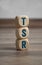Tower made of cubes and dice with acronym TSR Total shareholder return on wooden background
