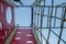 Tower, two walls of red with cutouts for climbing legs, grid of intertwined colored ropes, near hangs cable rope, on playground