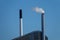 Towering industrial chimney blows harmful exhaust fumes into the clear blue sky.