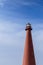 A towering red lighthouse ascends against a sweeping blue sky in Andenes, Lofoten